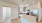 Bright kitchen with a large island with creamy grey quartz coutnertops, creamy grey cabinets, stainless steel appliances and an office entrance off to the right side of the photo