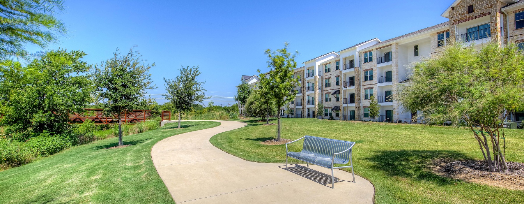 Sidewalk trail surrourinded by grassy area with apartment builkding in the backgriound
